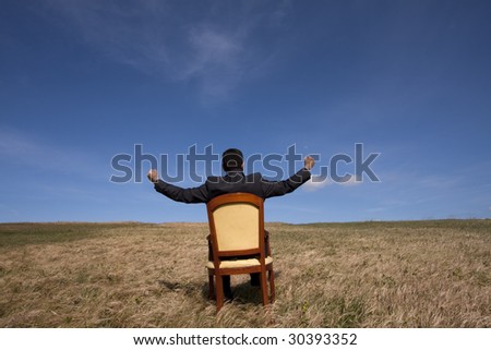 businessman in the field sited in a chair with his arms outstretched