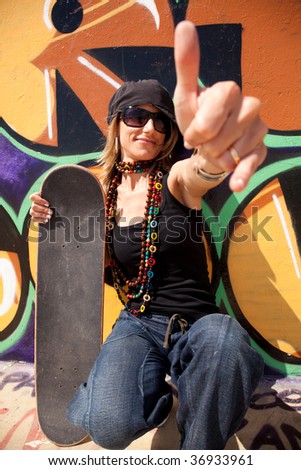 cool skateboard woman next to a graffiti wall. The Graffiti is illegal art in a public park.