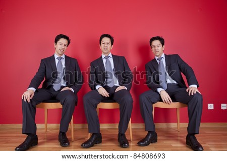 three confident businessman relaxing in a chair, next to a red wall