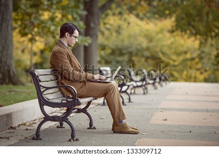 Positive Young Man Multitasking On A Park Bench