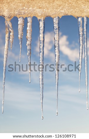 Icicles in the sunny day against a blue sky with white clouds.