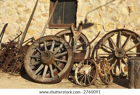 pile of old cart wheels and farming implements against stone wall
