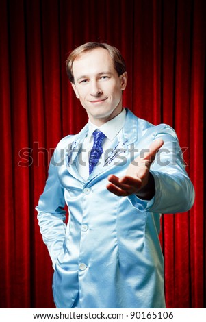 Funny smiling man dressed in a blue suite for a party showing his hand presenting something on a red background