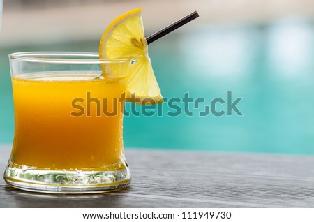 Glass of orange juice with orange slice with pool background
