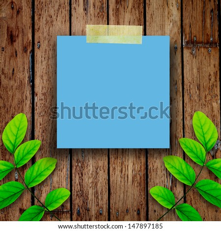 Blue paper note and green leaves on the old wooden background