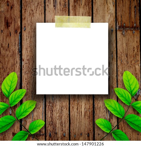 White paper note and green leaves on the old wooden background