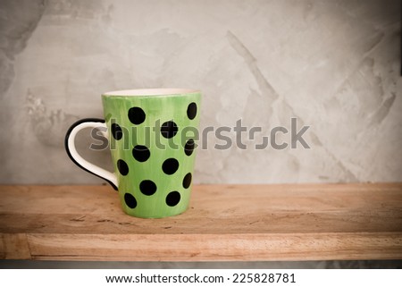 Green cup with dot on wooden background and cement wall.