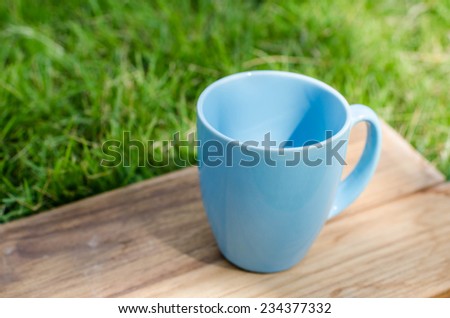 Blue mug on wooden board with green grass space.