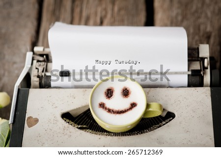 Happy Tuesday on typewriter with happy face coffee cup, sepia tone.