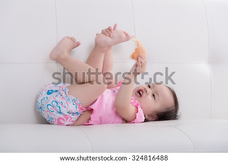 Cute Asian baby lying on sofa and eating bread at home.