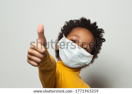 Happy African American black kid in medical protective face mask showing thumb up on white