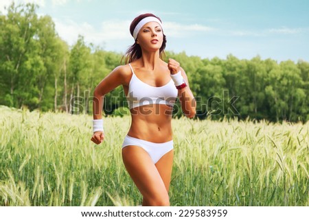 Young woman in white clothing running at field of high grass and forest.