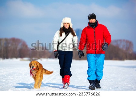 Young couple walking with dog. Cold winter season and snowfield.