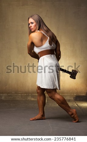 Young strong woman bodybuilder in white clothing with heavy hammer. Ancient style.