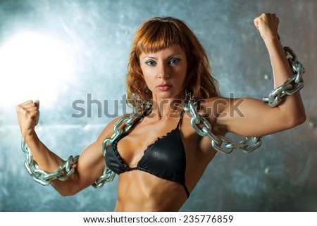 Young sexy sports woman in black lingerie with heavy chain on metallic wall background.