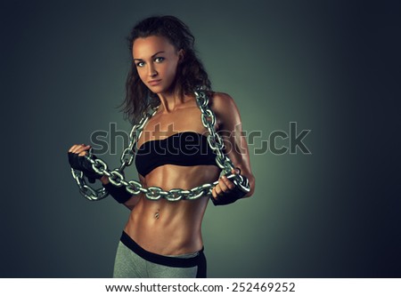 Young sports sexy brunette woman with heavy chain posing on wall background.