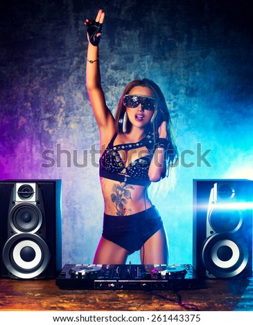 Young sexy woman dj playing music. Big loud speakers, headphones and dj mixer on table.
