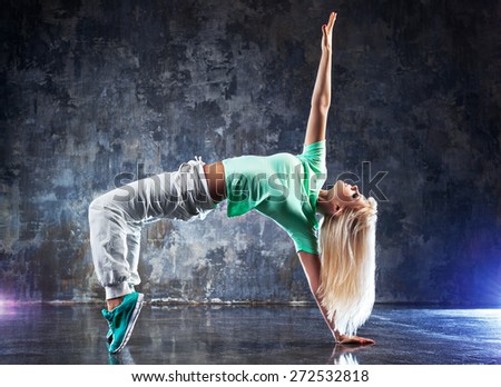 Young woman modern dancer. On dark stone wall background.