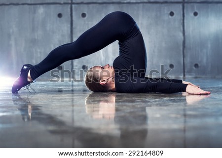 Strong woman gymnast in black clothing stretching upside down on wall background.