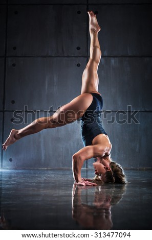 Strong woman bodybuilder standing upside down on wall background.