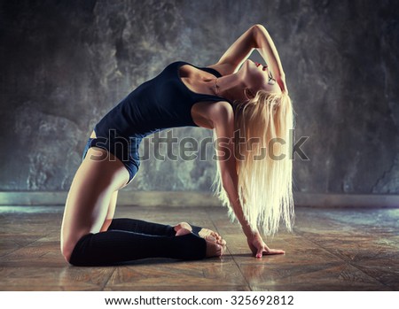 Young woman dancer in black clothing on wall background.