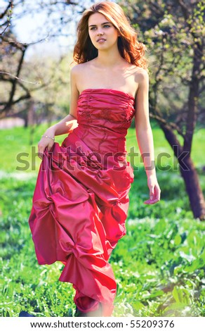 Young woman in red dress walking in garden.