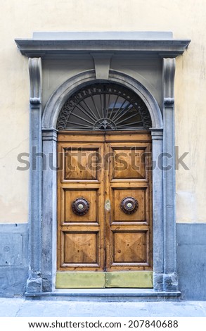 An old wooden double door with ornate handles surrounded by a carved stone decorative frame in a cement rendered wall.