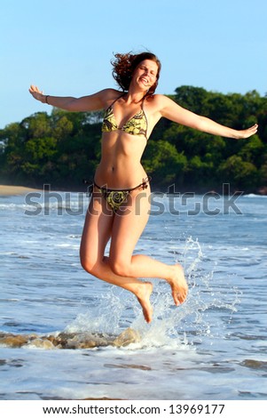Joyful Jumping A young woman at the beach in the water. Jumping for joy with a bikini.