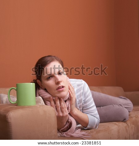 A young woman is sick. She is lying on the couch and is sneezing. She has a tea. A lot of copyspace.