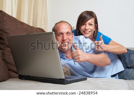 Young couple on the couch at home looking at the laptop! They both give a thumbs up sign!