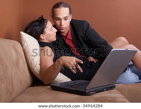 Young couple on the couch surfing the web with their laptop - showing a thumbs up sign.