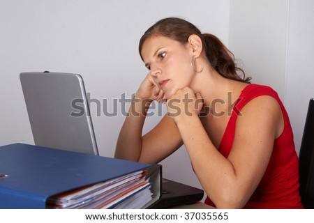 Young woman sitting at her laptop with a lot of work in front of her. She is very frustrated.