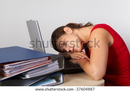 Young woman is sleeping at her laptop with a lot of work in front of her.