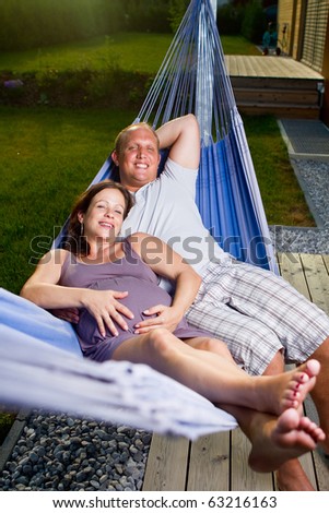 Young loving couple in a hammock in a summer setting. The woman is pregnant.