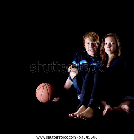 Young teenage couple in love with a basketball next to them. Isolated over a black background.