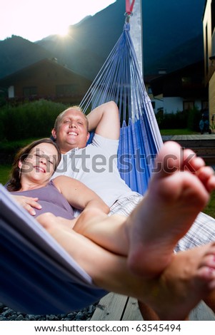 Young loving couple in a hammock in a summer setting. The woman is pregnant.