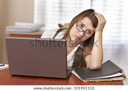 Frustrated and tired young lady with small workload sitting behind laptop