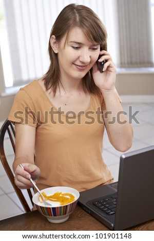 Lady sitting at laptop and chatting on cellphone while eating healthy food