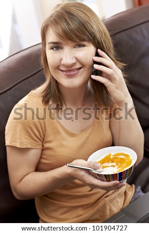 Happy young lady chatting on cellphone while holding a bowl of healthy food