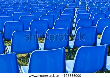 multitude of empty blue chairs in a park before a concert