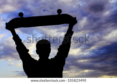 Youth boy expressing himself with raised skateboard gesture while looking at a very vivid sky with striking cloud formation (silhouette).