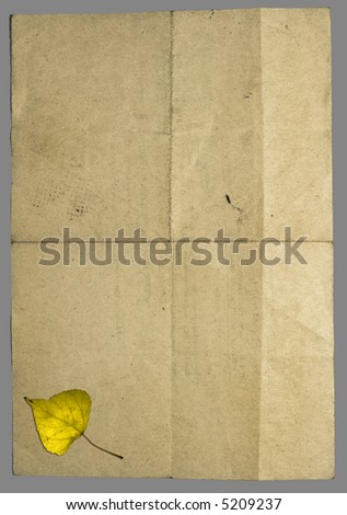 Vintage crumpled retro style paper with many folds and with yellow fallen autumn leaf in lower part. Image isolated on grey with clipping paths