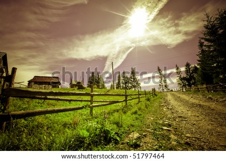 Colored mist rural landscape with road and fence on foreground and farm with sky above on background.