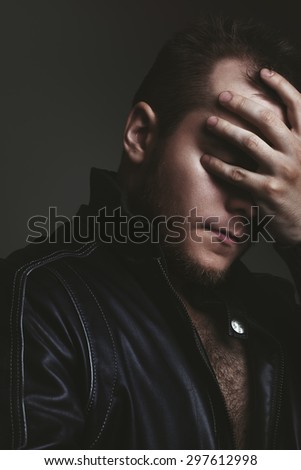 unshaven man in a black jacket covered his face with his hand