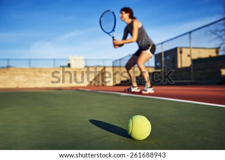 a tennis ball and young woman holding a tennis racquet in background.  focus on tennis ball.