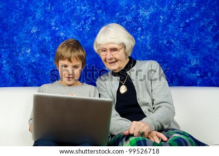 Grandmother and grandchild sitting in a sofa looking at a laptop