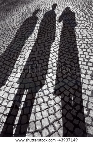 Shadows of three people in coats on cobble-stone pavement