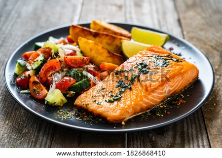Fried salmon fillet with fried potatoes, lime and vegetable salad served on black plate on wooden table