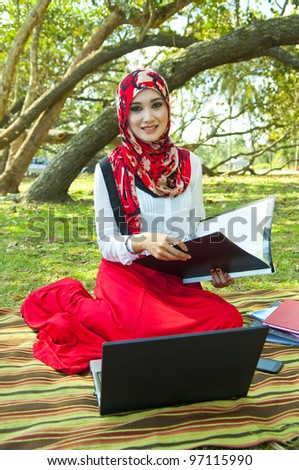 Beautiful muslim woman wearing scarf with notebook at a garden