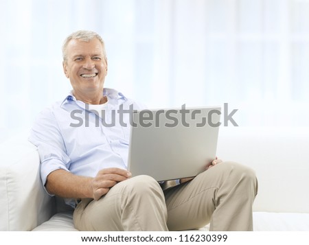Portrait of a happy senior man sitting on couch and using his laptop